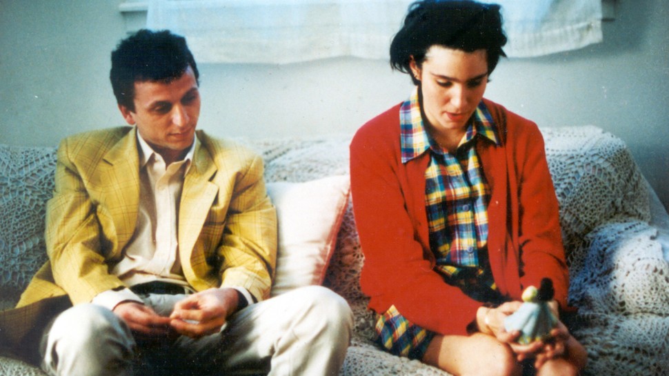 a young man in a yellow jacket and a young woman in a red jacket sit next to each other on the couchalr