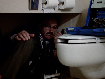 Gene Hackman crouched beside a toilet with audio equipment